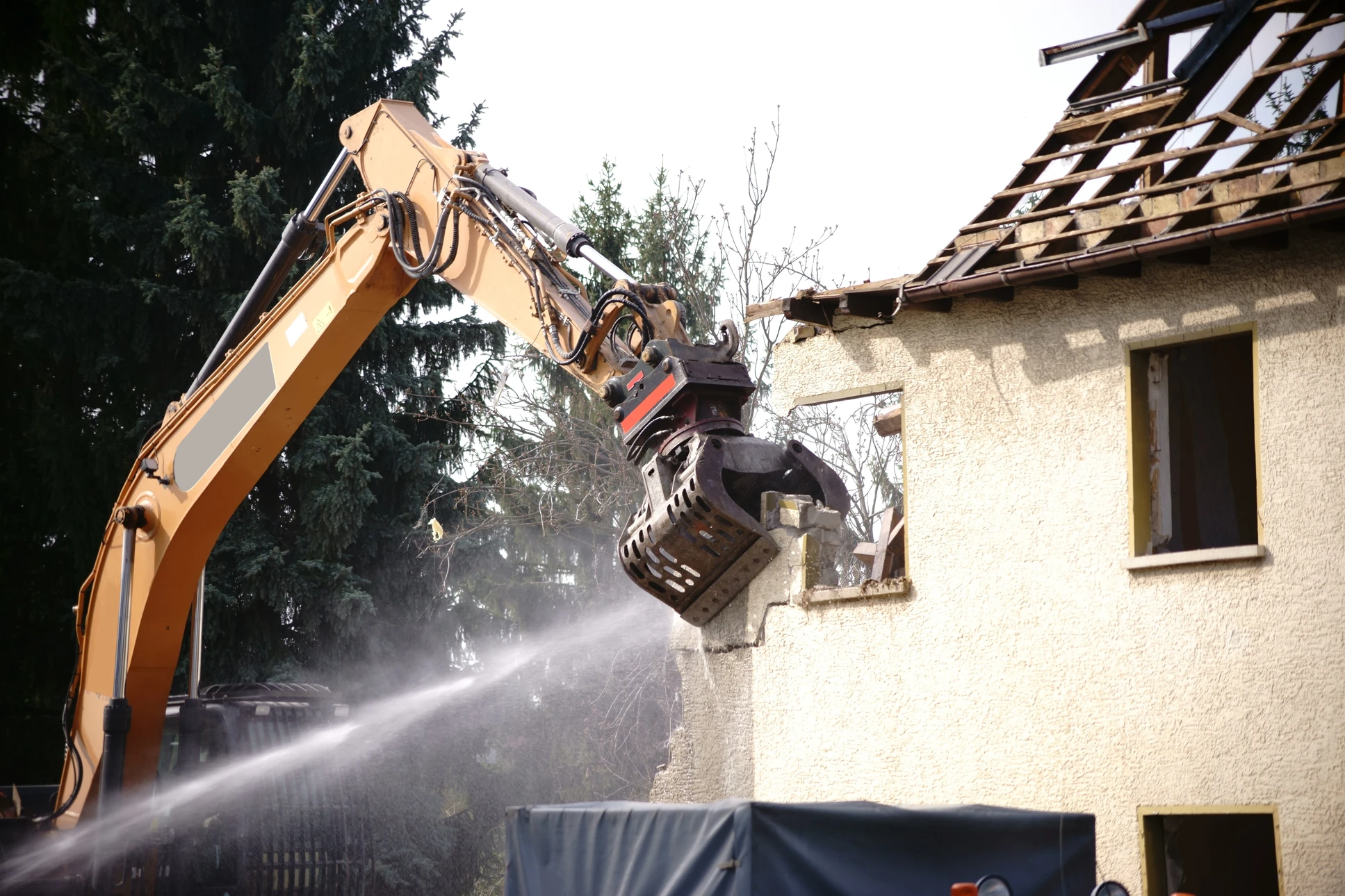Chantier de démolition en extérieur avec pelleteuse hydraulique équipée d'un godet-pince démolissant une maison résidentielle