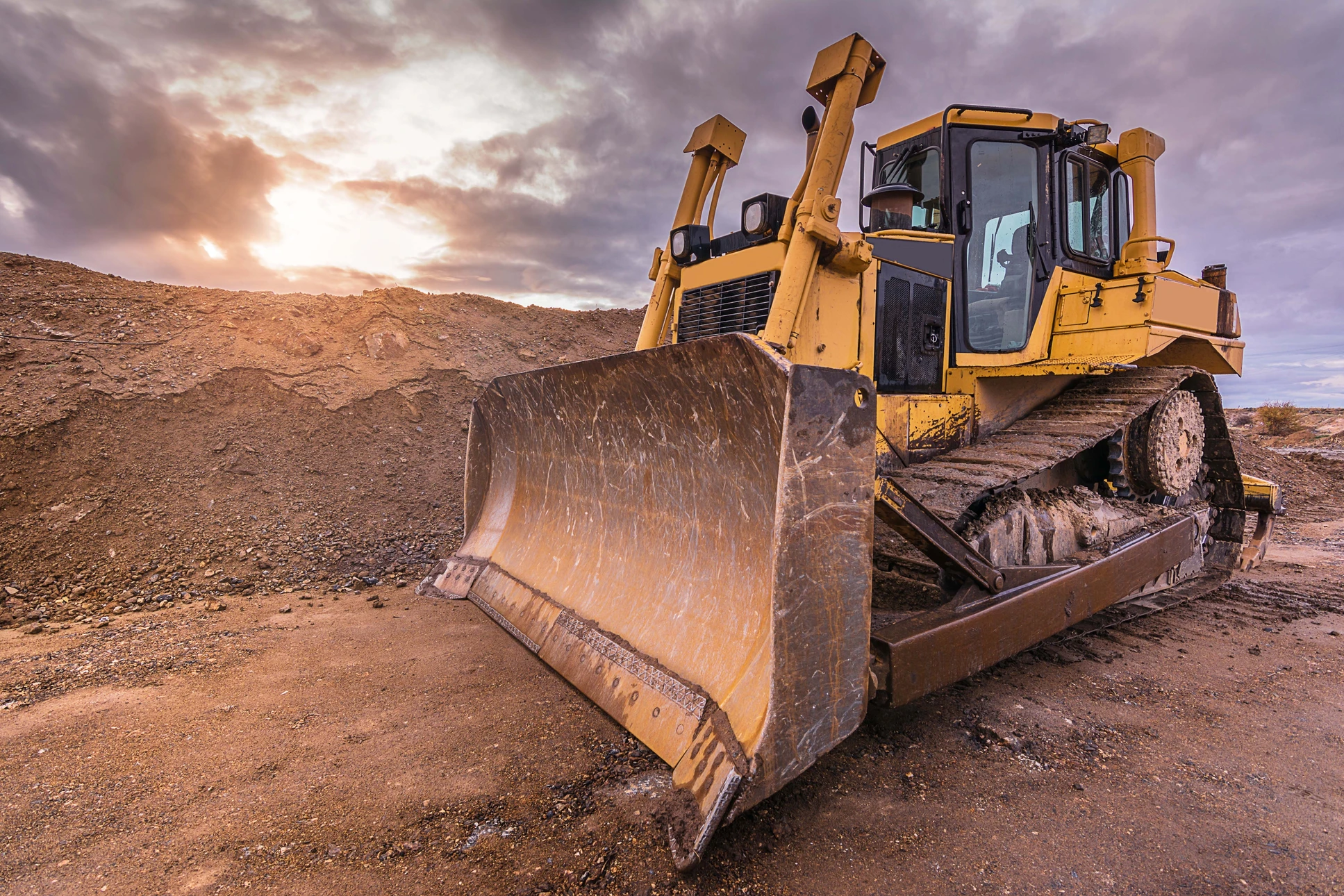 Chantier de terrassement en extérieur avec bulldozer jaune sur terrain aride sous ciel nuageux au coucher du soleil