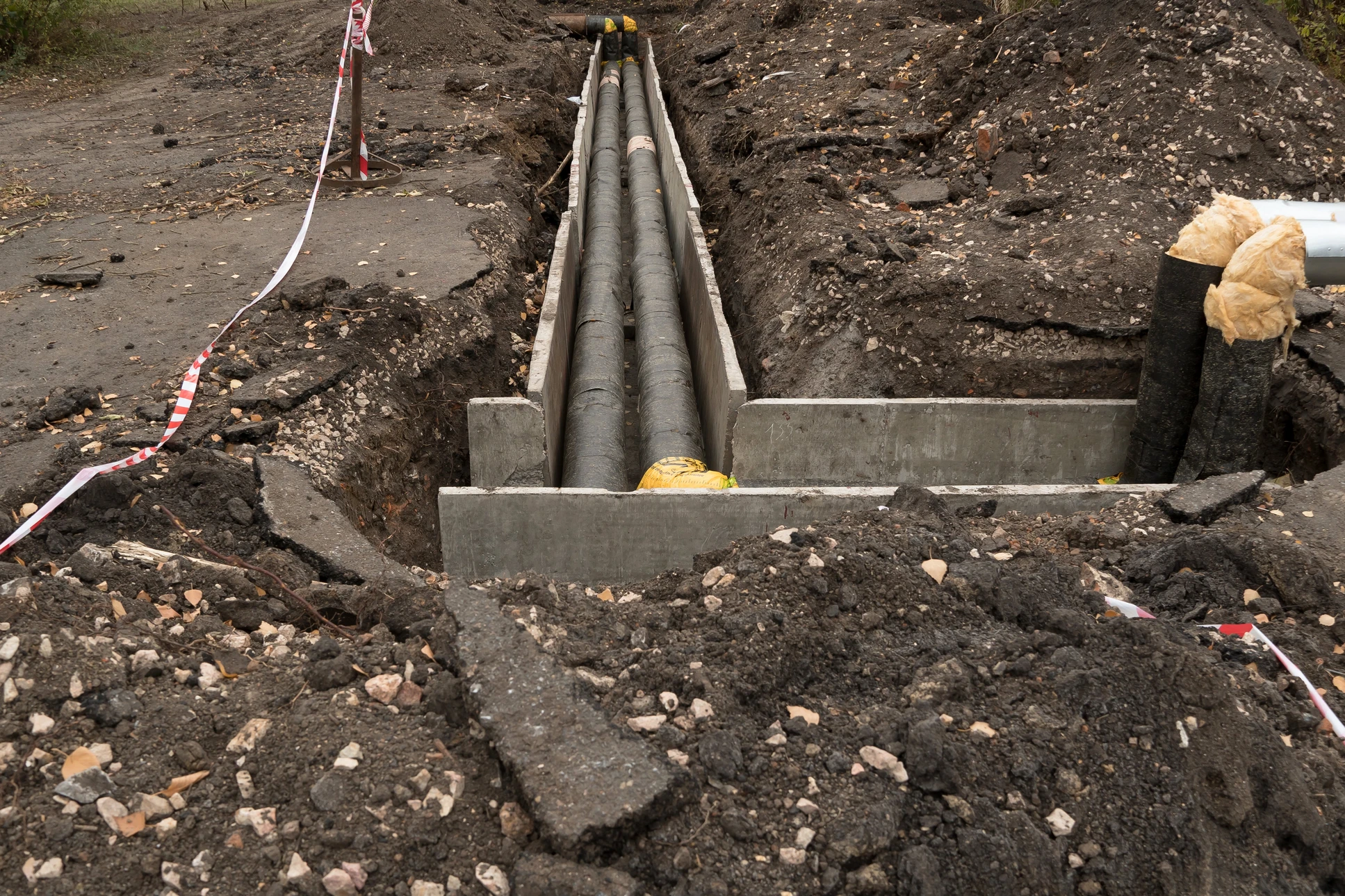 Chantier de travaux publics en extérieur avec tranchée ouverte et canalisations grises installées dans coffrages béton préfabriqués