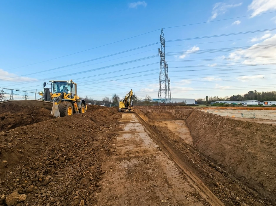 Chantier de construction extérieur au coucher de soleil avec opérateurs utilisant une foreuse hydraulique sur chenilles et un compacteur à roues